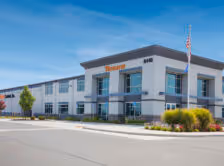 Modern two-story commercial building with Tormach signage, clear blue sky, and landscaping at the entrance.