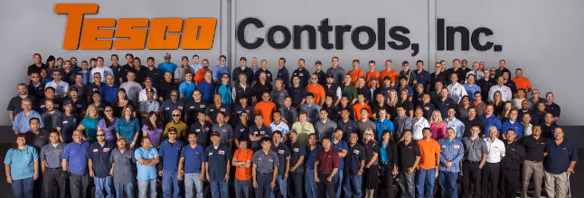 Large group of Tesco Controls, Inc. employees posing in front of a wall with the company logo.