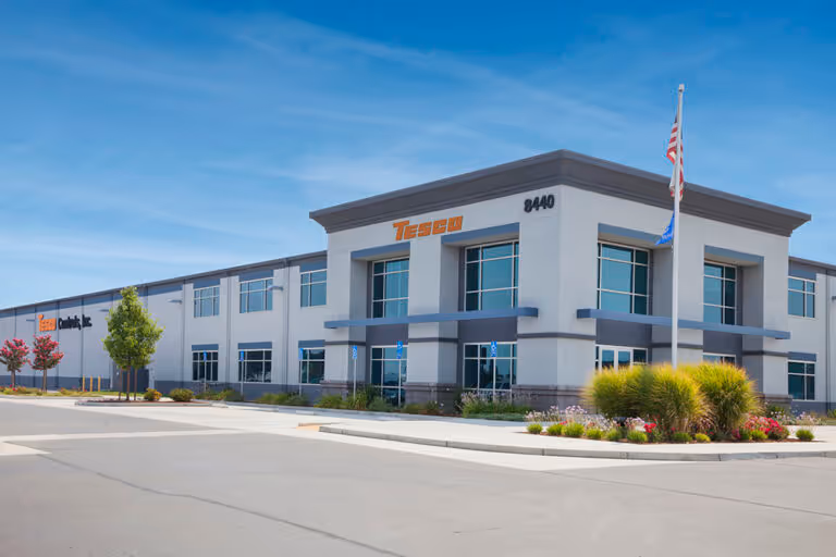 Modern corporate building with Tesco Controls Inc. logo, address number 8440, and an American flag on a flagpole in front.