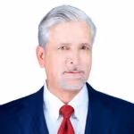 Mature man with gray hair and beard wearing a navy blue suit, white shirt, and red tie, against a white background.