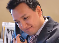 Man in a suit and checked tie talking on a office phone handset with a slight smile.