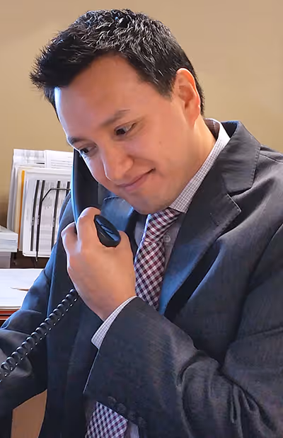Businessman in a suit speaking on a desk phone, looking focused and smiling slightly.