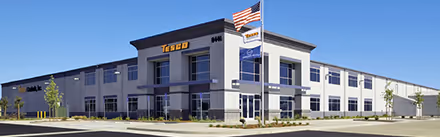 Modern two-story Tesco corporate office building under clear blue sky with American and Tesco flags.