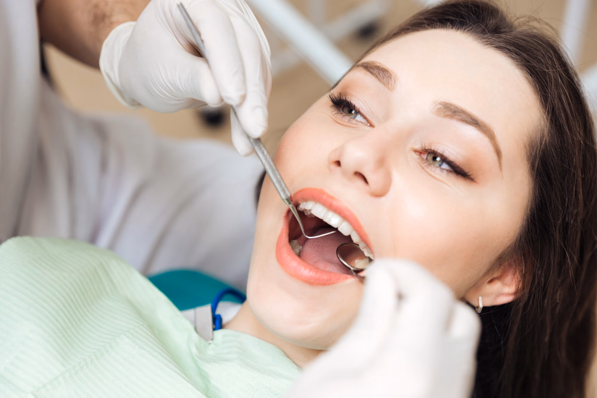 Female patient receiving a routine dental examination with dental instruments.