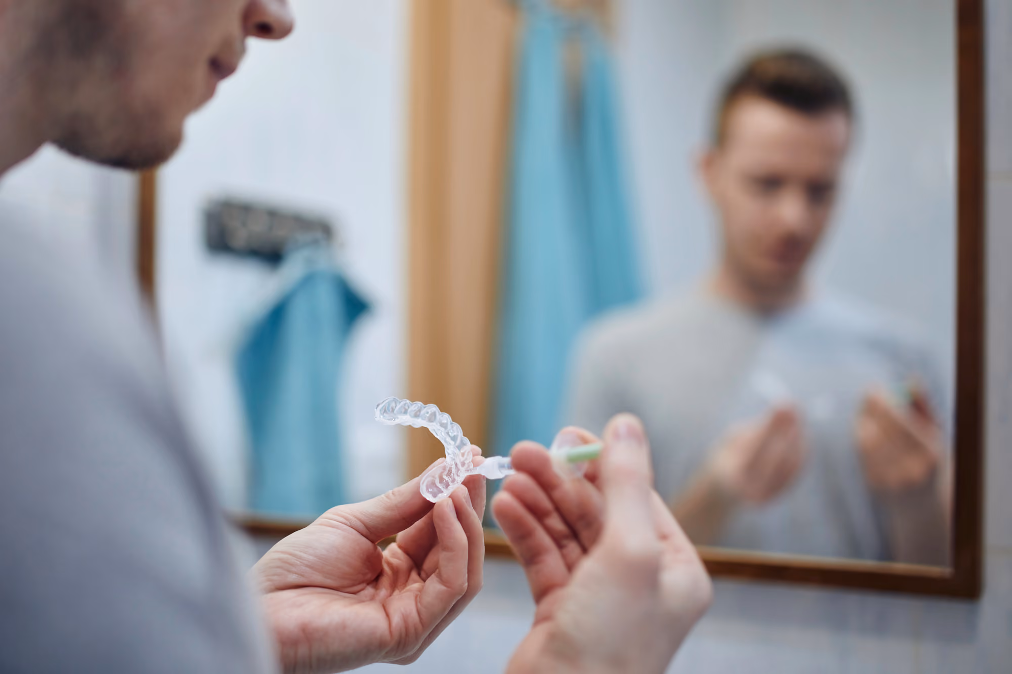 Person cleaning clear aligners with a toothbrush in front of a bathroom mirror.