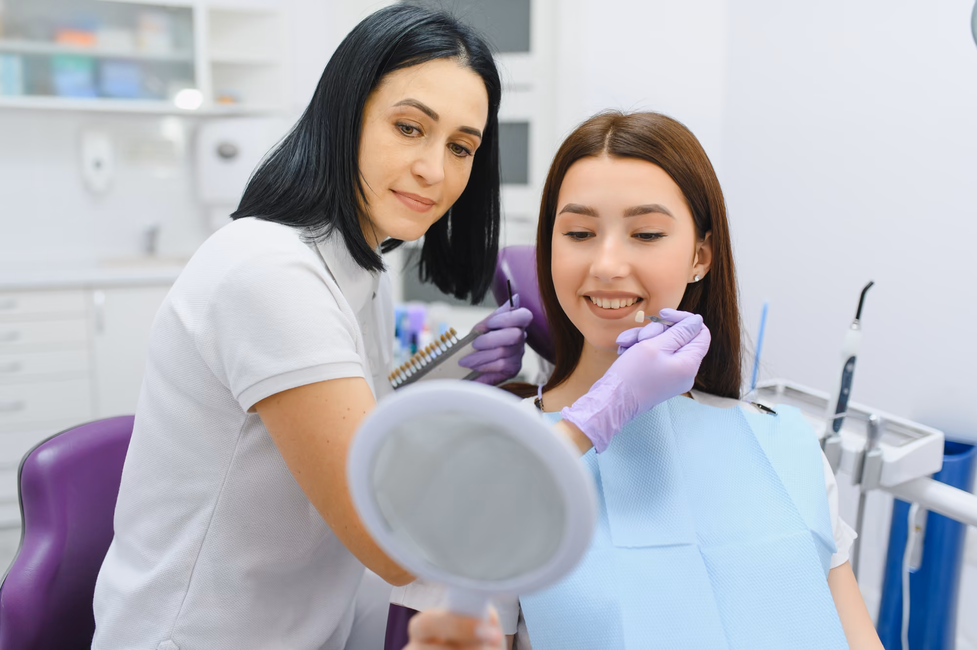 Dental professional helping a patient review smile results using a handheld mirror.
