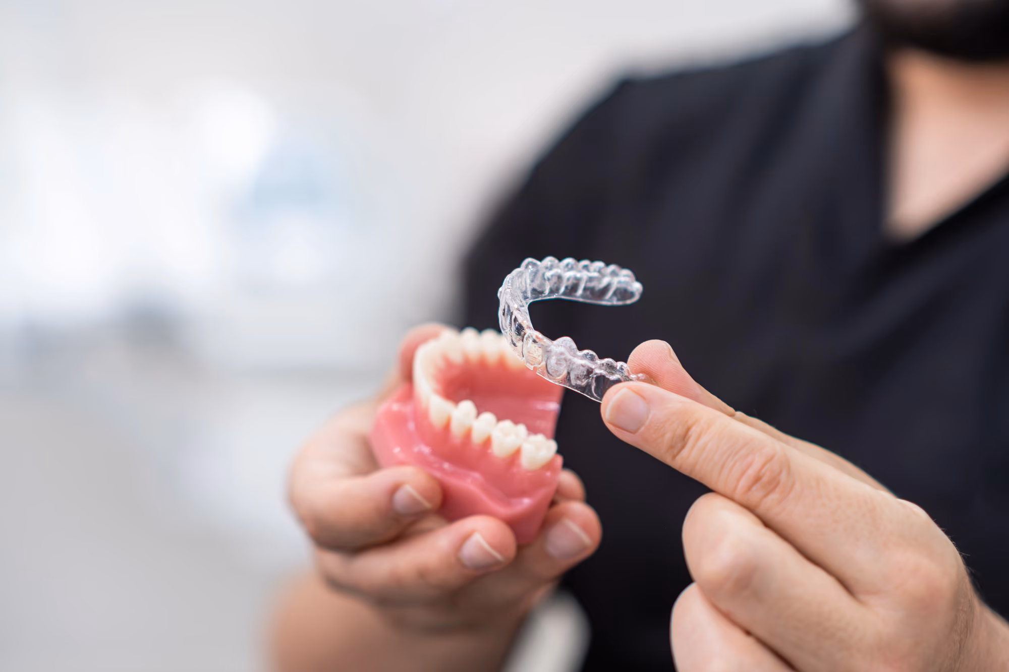 Dentist demonstrating a clear aligner using a dental teeth model for comparison.