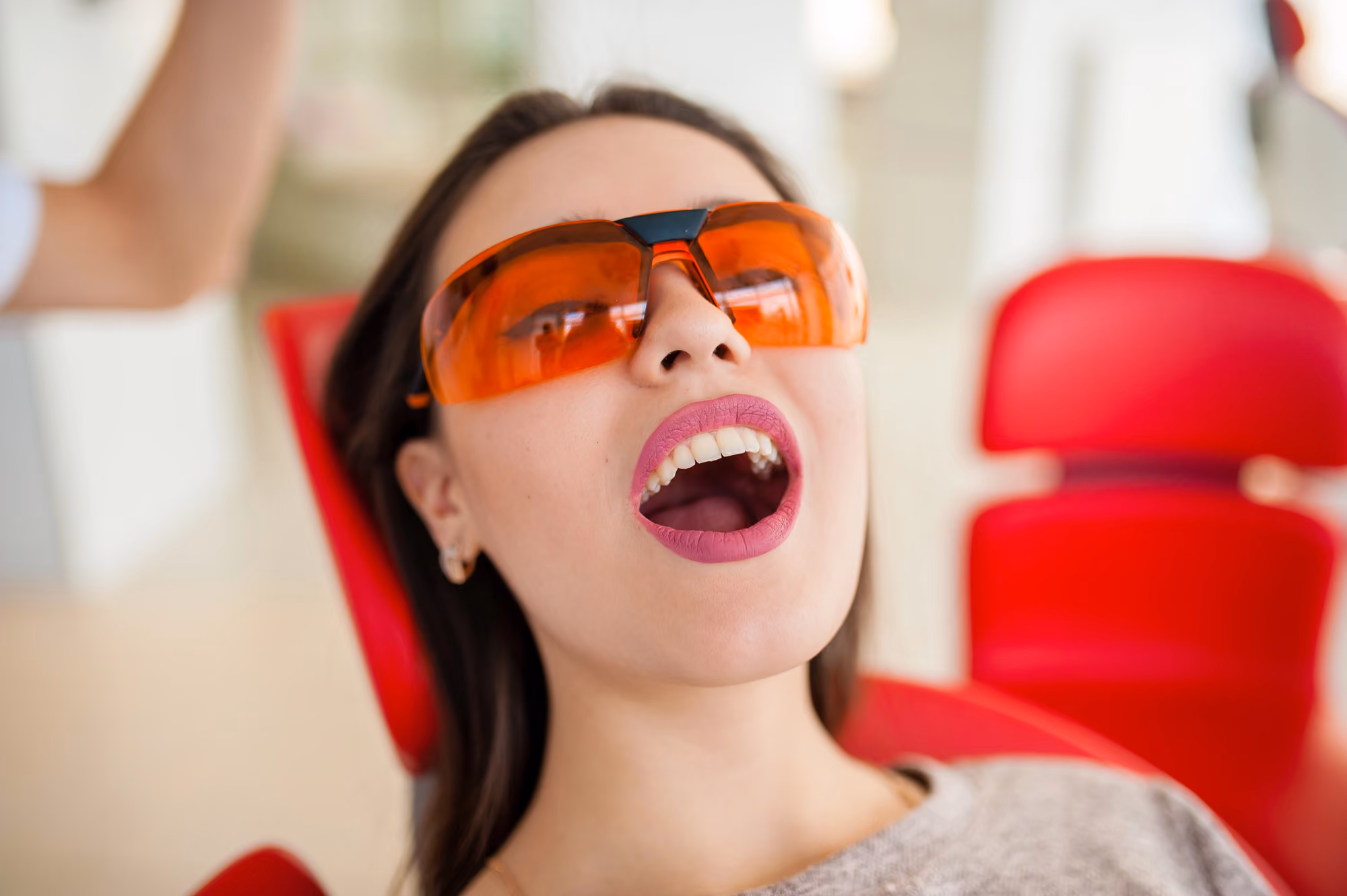 Patient wearing protective glasses smiling with mouth open during a dental visit.
