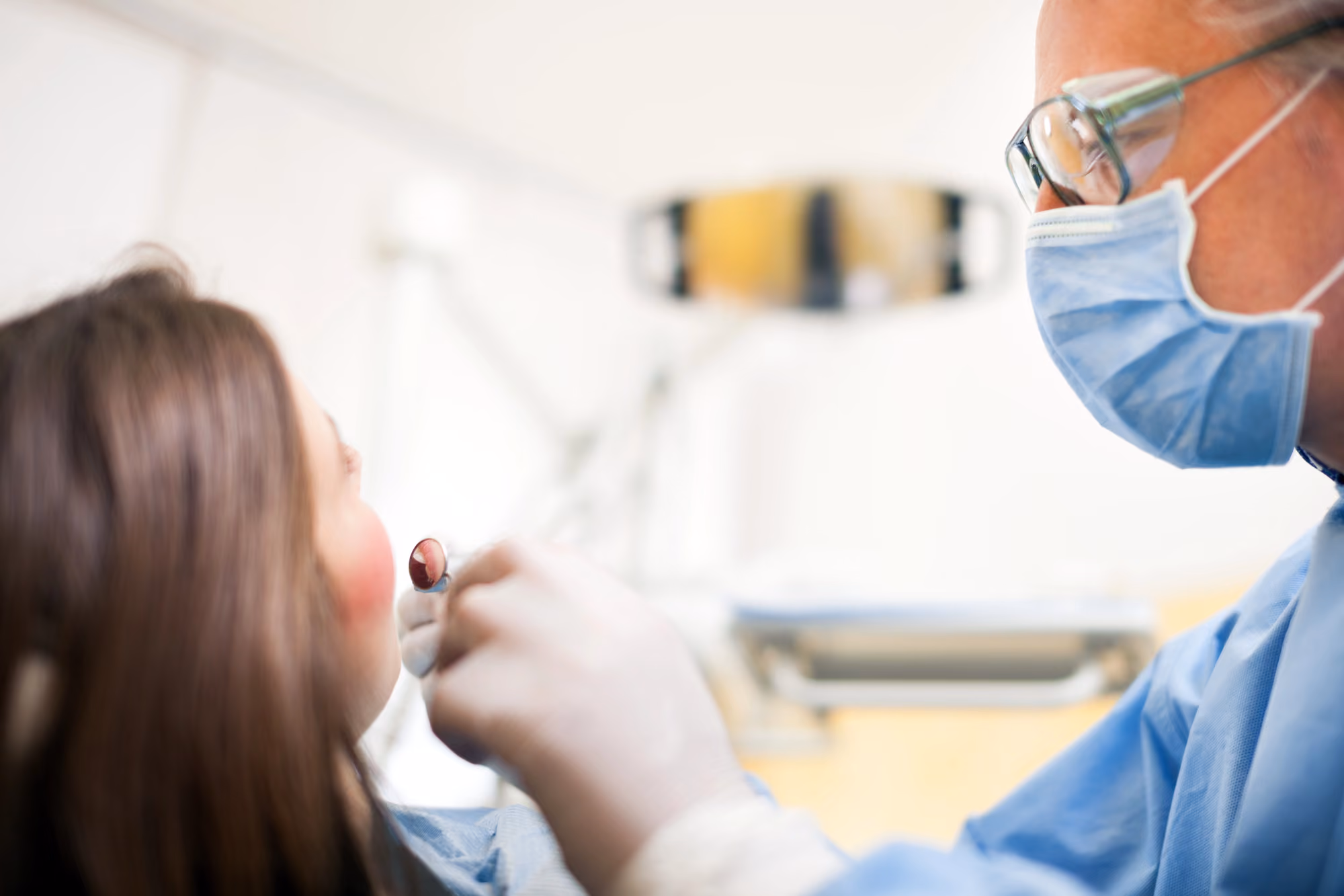 Dentist performing an oral cancer exam on a patient wearing protective eyewear.