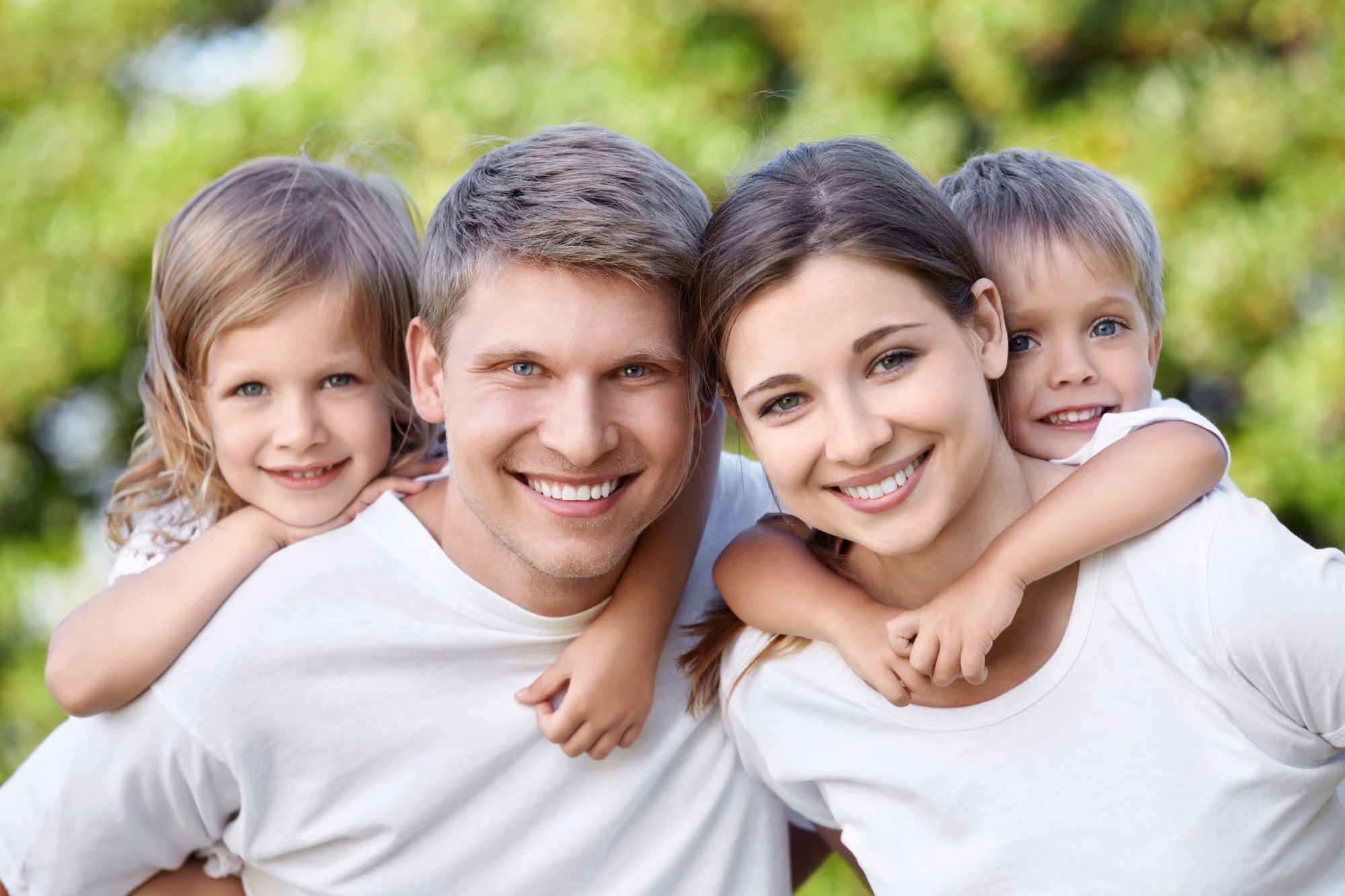 Smiling family of four posing together outdoors in a park setting.