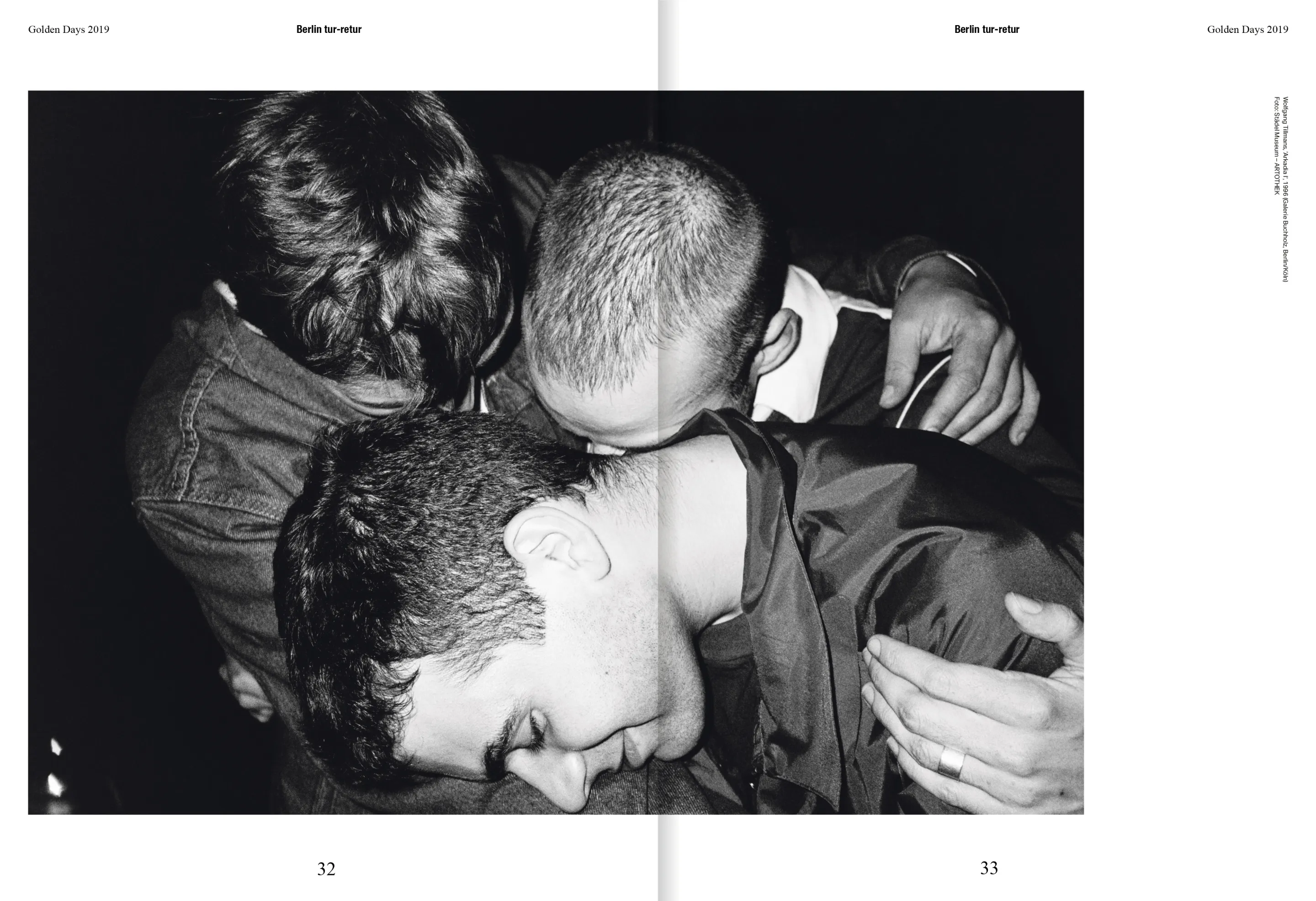 Black and white photograph of three men in a close embrace, heads bowed together in an intimate moment.