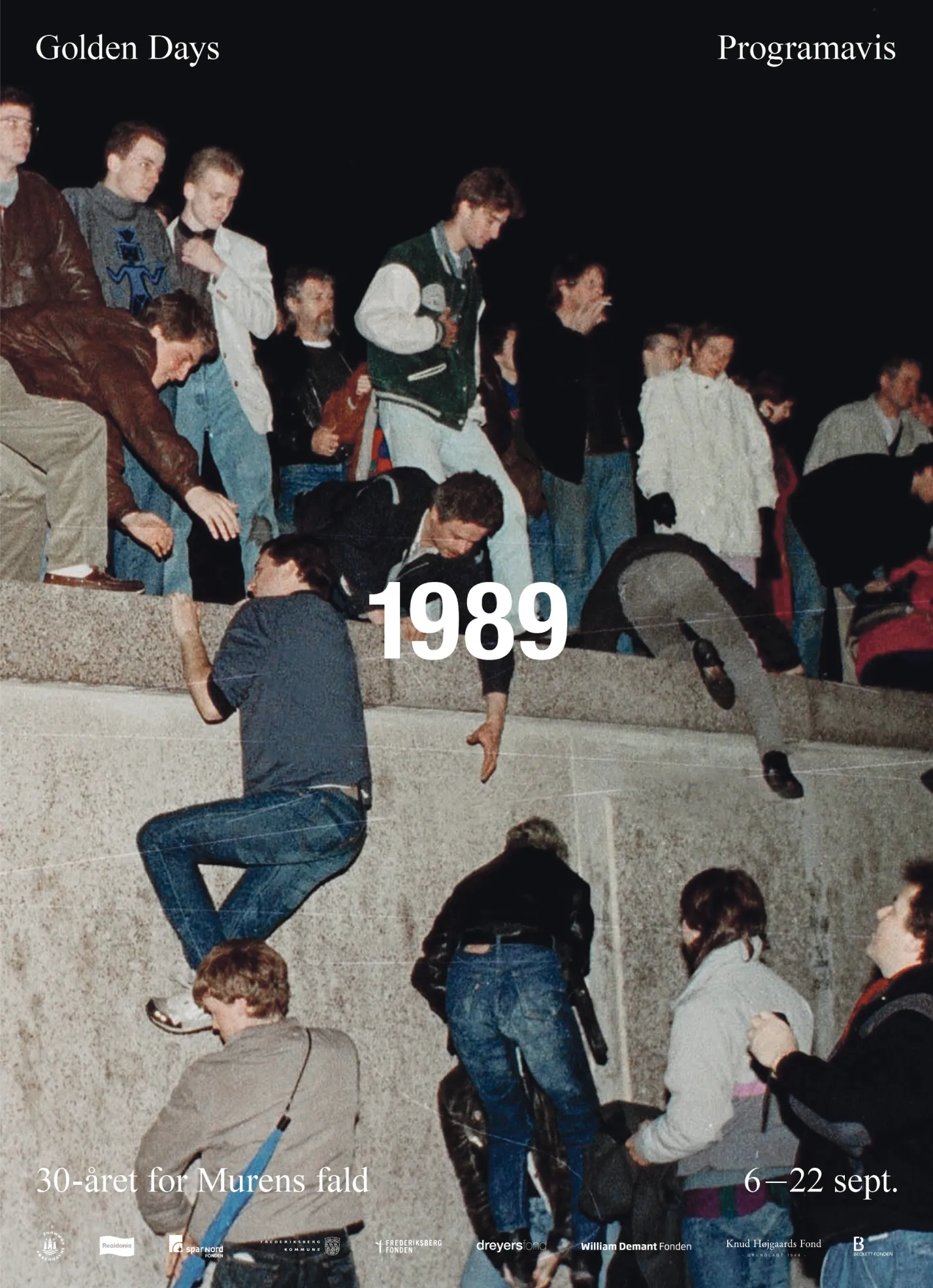 People climbing and helping each other over a concrete wall at night in 1989 during the fall of the Berlin Wall.