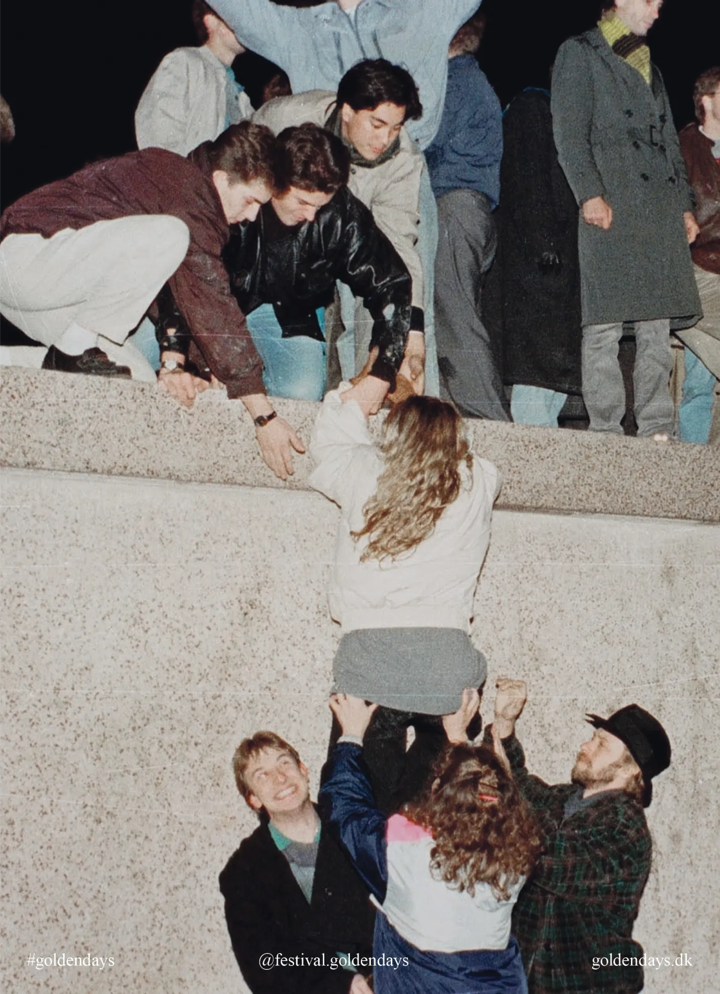 Group of people helping a woman climb up a concrete ledge at night during a festival.