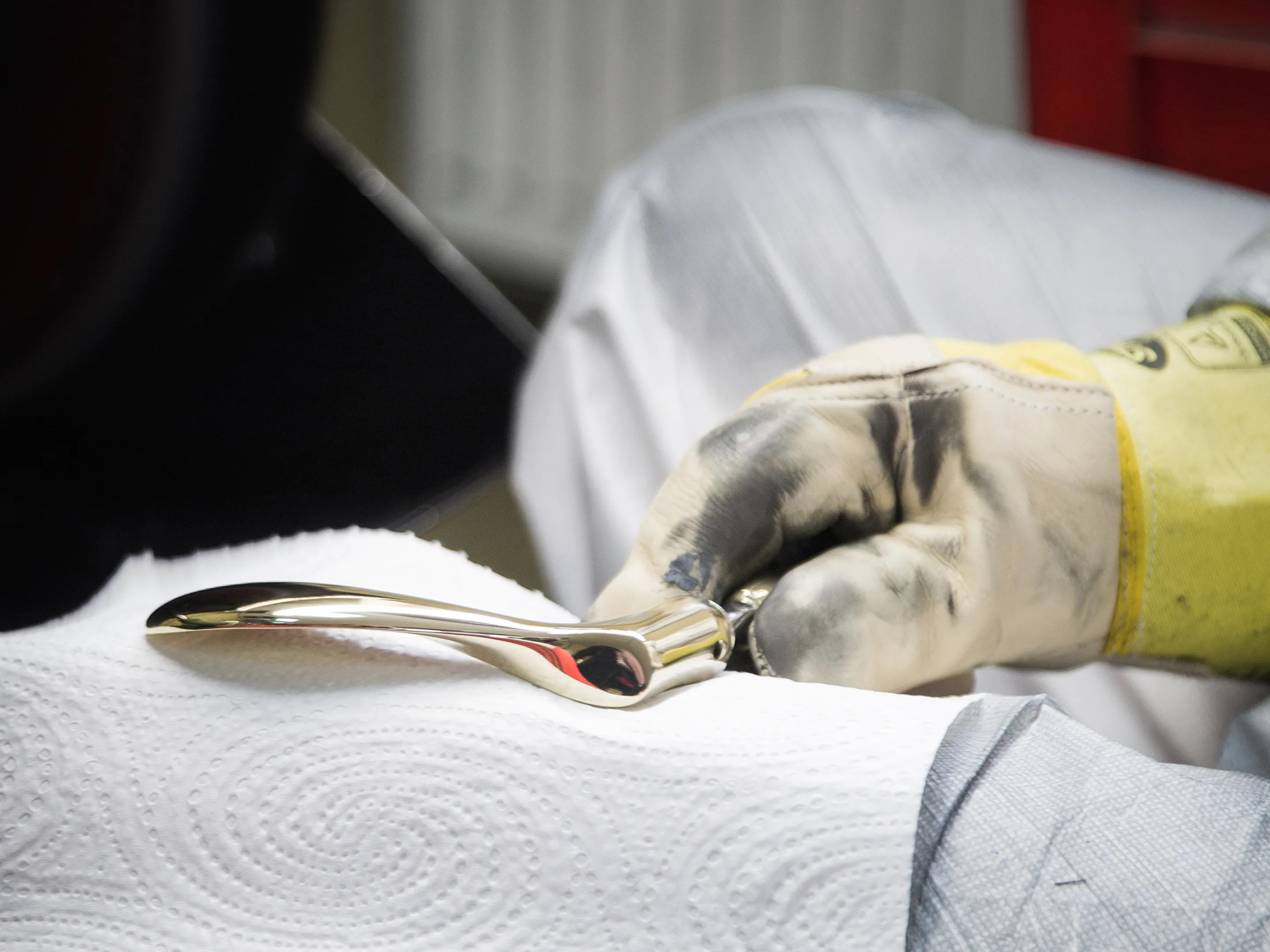 Person wearing dirty work gloves holding a shiny, curved metal door handle wrapped in paper towel.