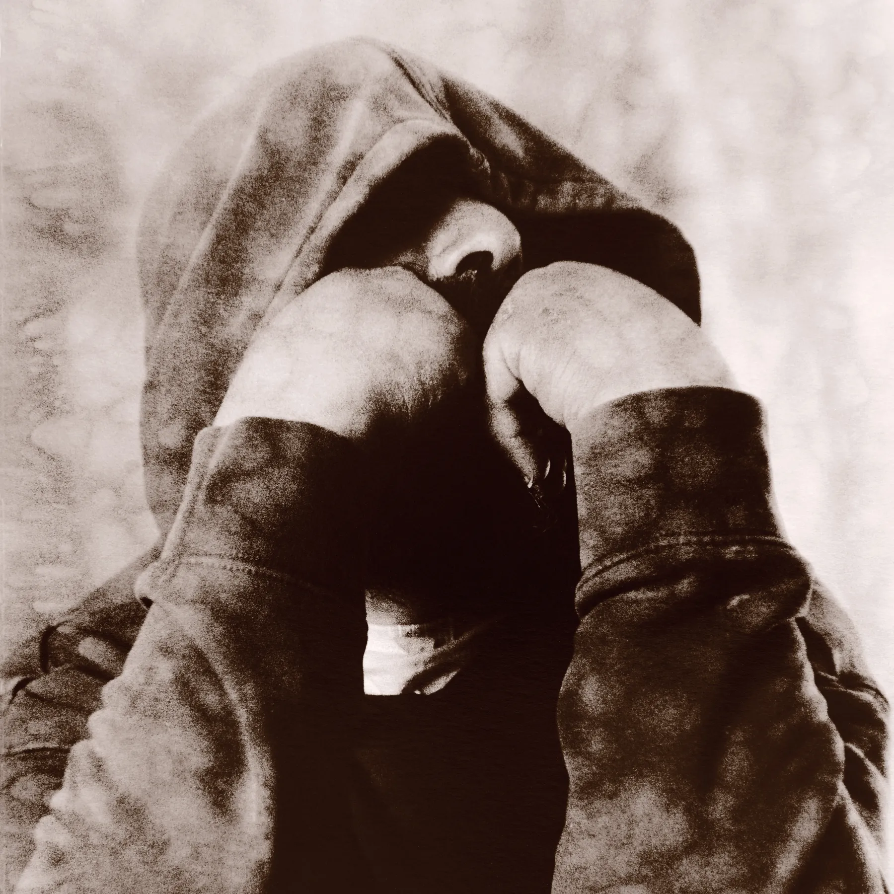 Person in a hooded jacket with fists raised close to their face, in a sepia-toned image.