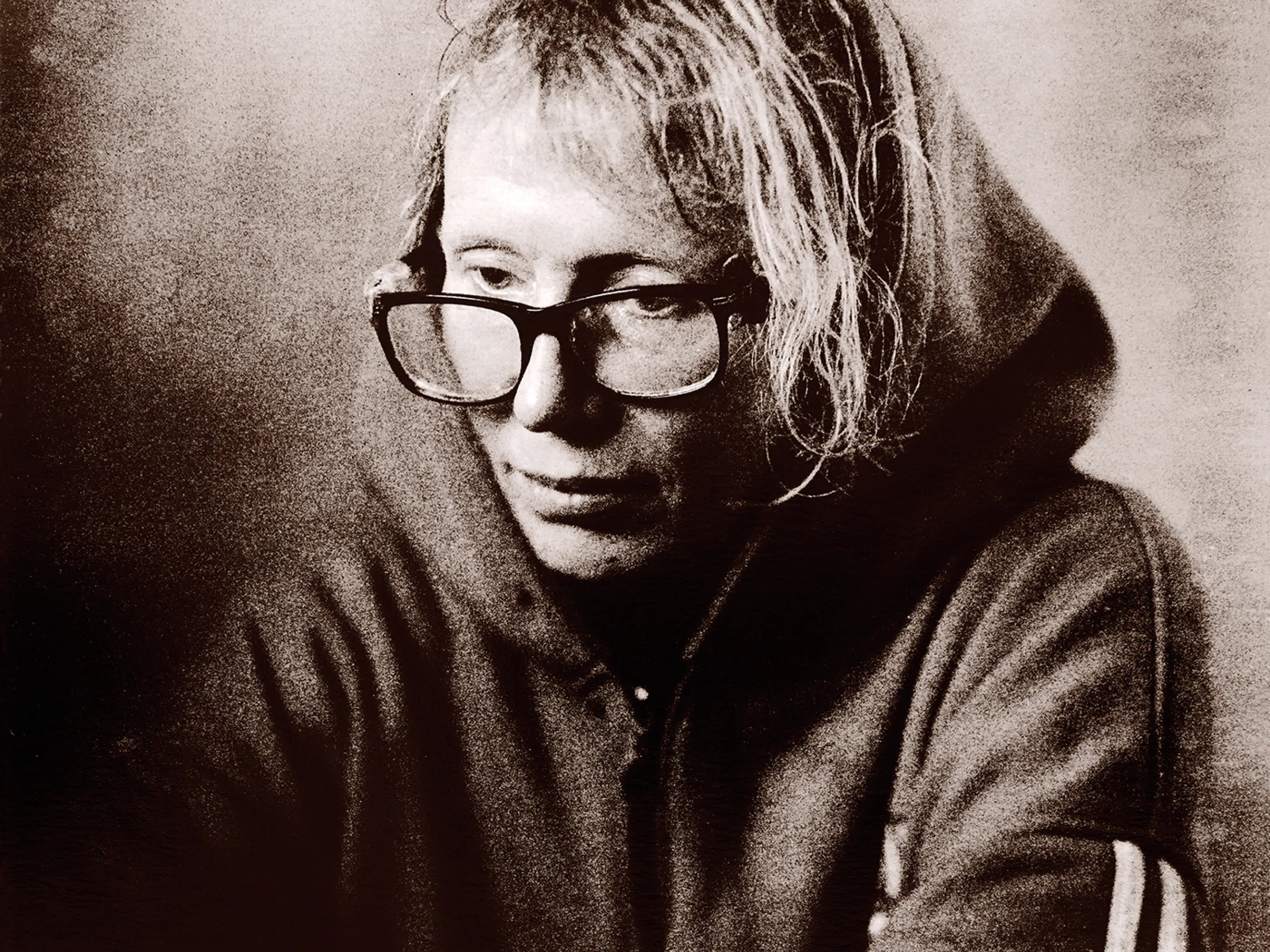 Black and white portrait of a person with glasses wearing a hooded sweatshirt, looking pensive.