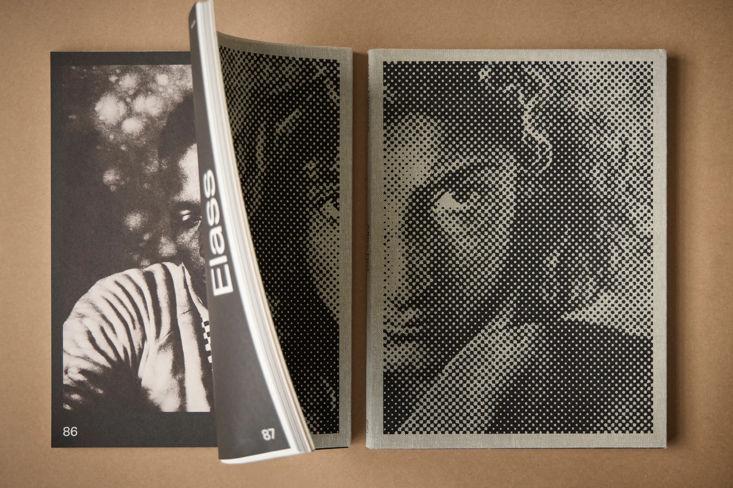 Two open books lying on a brown surface, each showing a black and white halftone portrait of a person's face.