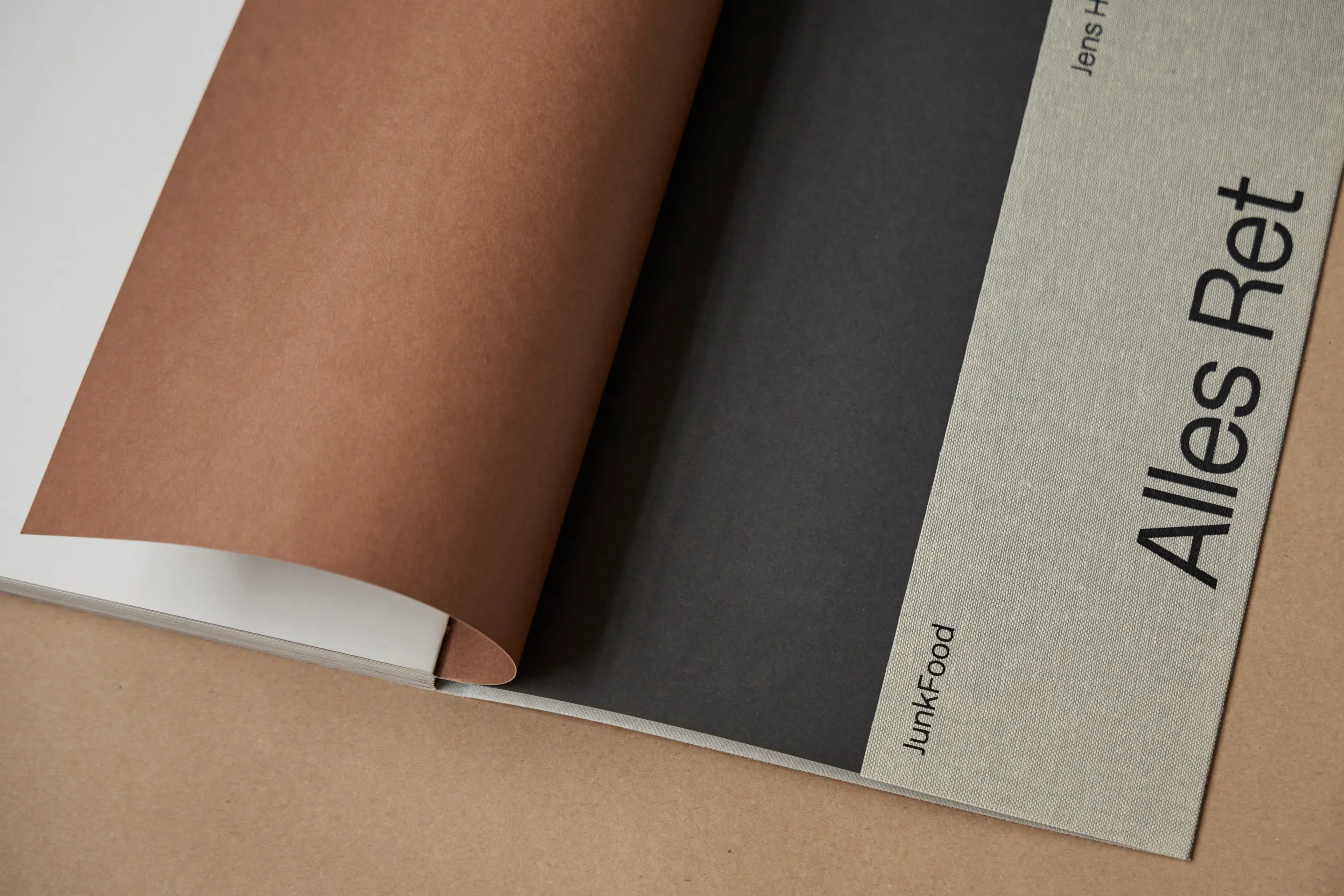 Partially opened book showing pages in brown, black, and beige with text 'JunkFood' and 'Alles Ret'.