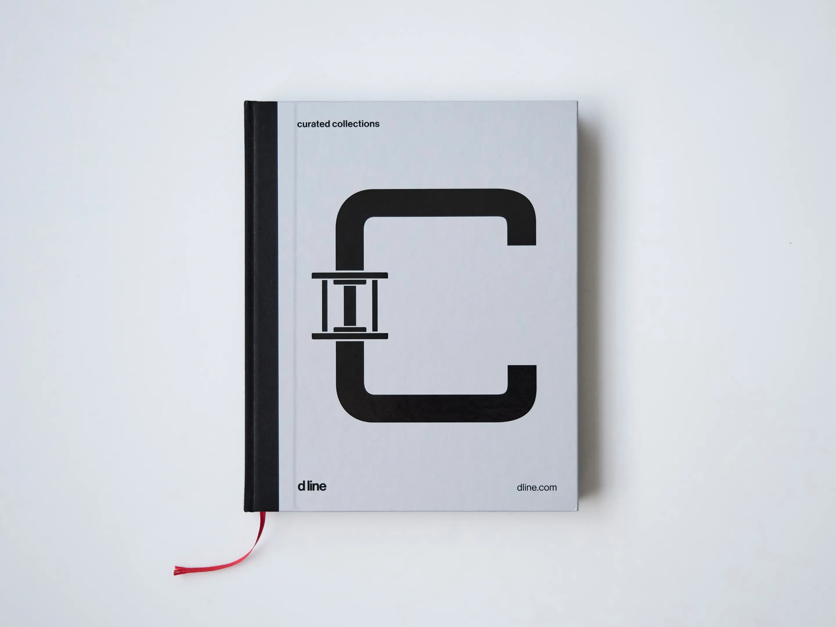 Closed book with a minimalist black design on the cover, black spine, and a red ribbon bookmark on a white background.