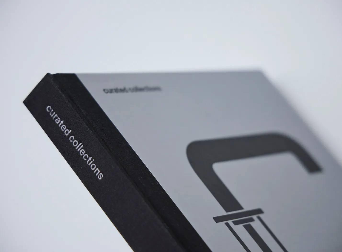 Close-up of a book spine and cover with the title 'curated collections' on the spine and a partial black graphic on the gray cover.