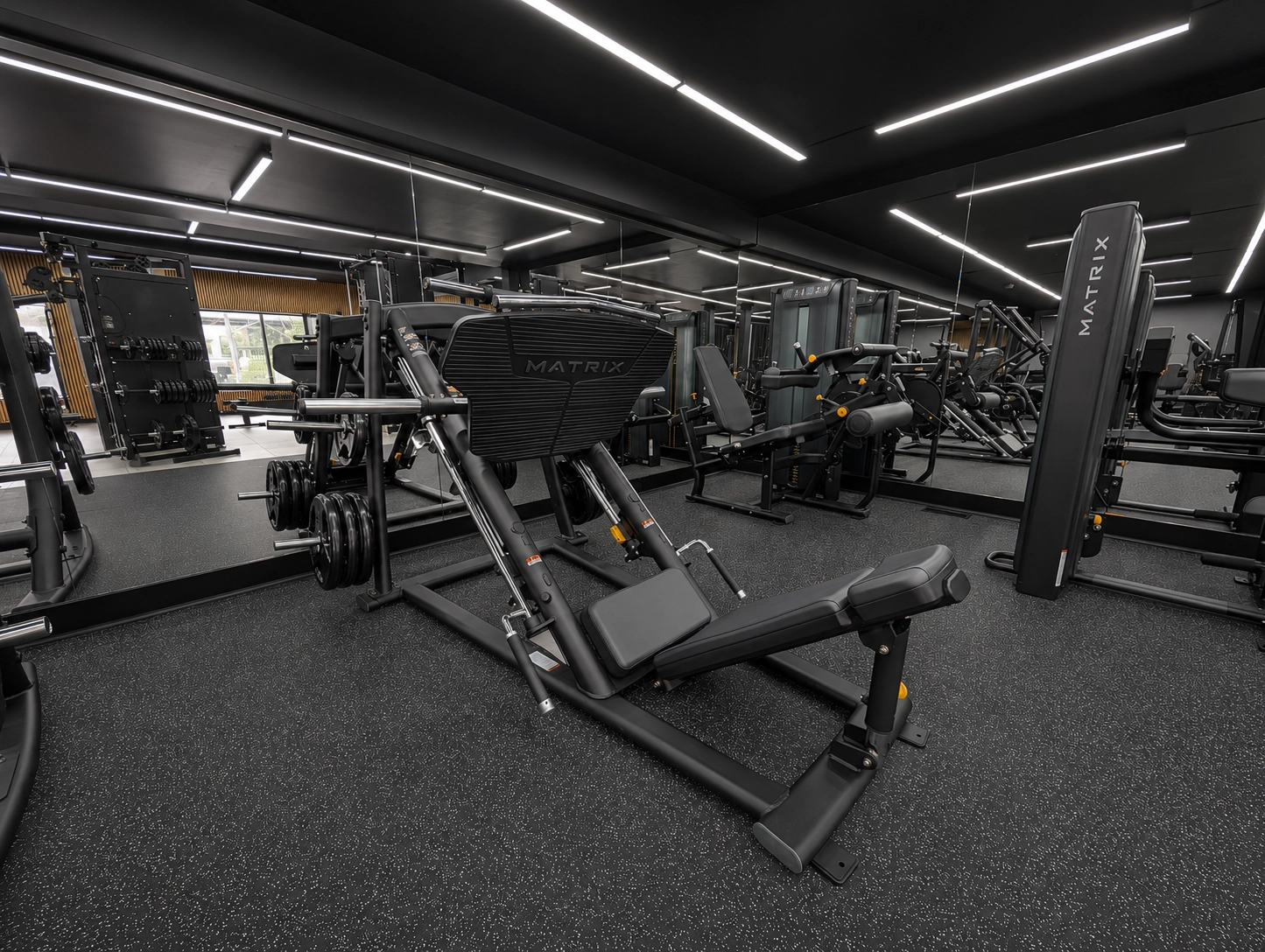 Intérieur d'une salle de sport moderne avec des équipements de musculation, un sol noir avec des éclats, un plafond noir avec des lumières LED blanches en forme de lignes géométriques, et des personnes s'entraînant.