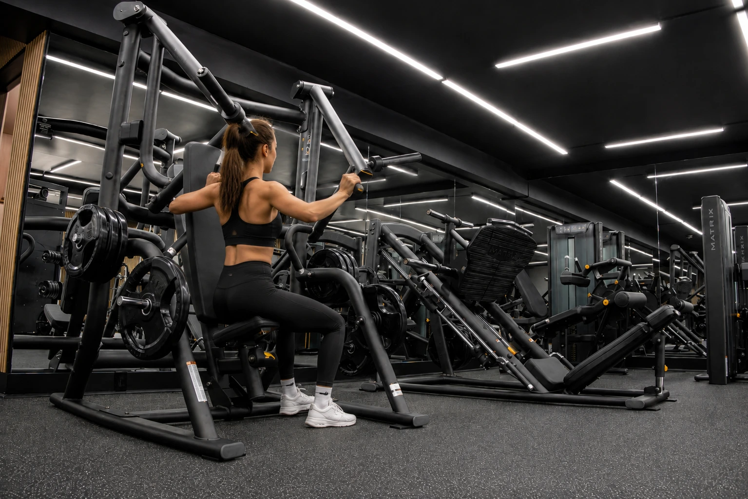 Femme en tenue de sport rouge courant sur un tapis roulant dans une salle de gym moderne avec machines d'exercice et vélos stationnaires.