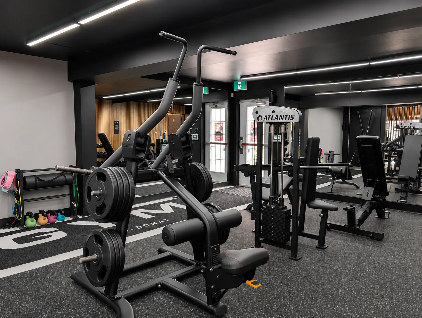 Intérieur d'une salle de sport moderne avec des équipements de musculation, un sol noir avec des éclats, un plafond noir avec des lumières LED blanches en forme de lignes géométriques, et des personnes s'entraînant.
