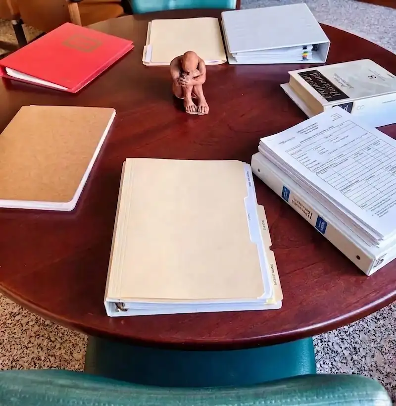 Mesa redonda de madera con documentos y carpetas en su perímetro y una figura en el centro