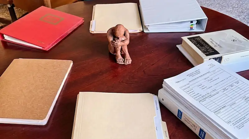 Mesa redonda de madera con documentos y carpetas en su perímetro y una figura en el centro