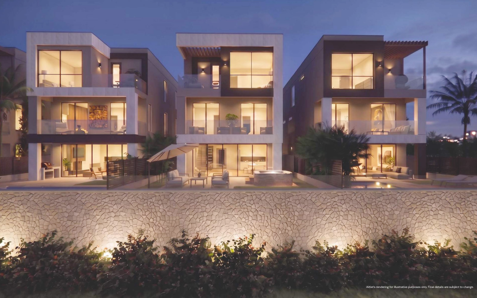 Three modern three-story houses at dusk with large illuminated windows, glass balconies, outdoor seating areas, and surrounding landscaping with a stone wall and plants in front.