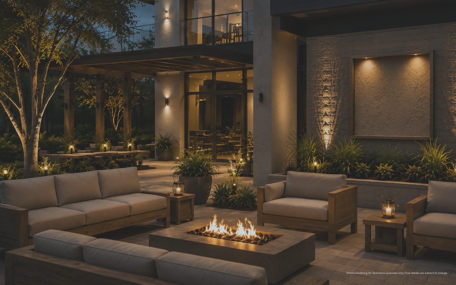 Outdoor patio at dusk with modern cushioned wooden sofas and chairs arranged around a rectangular fire pit, surrounded by plants, soft lighting, and a building with large glass windows in the background.