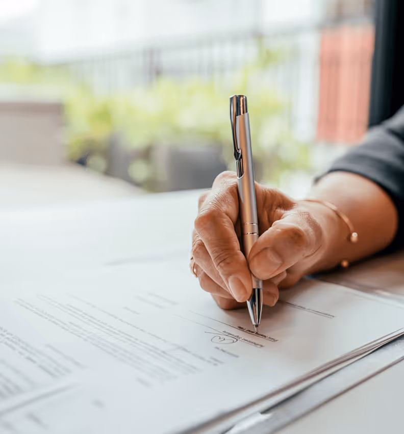 Hand unterzeichnet Dokument mit Stift, Fokus auf Unterschrift, im hellen Raum.