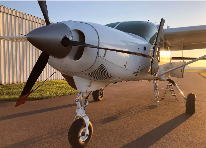 Cessna Caravan airplane parked on a runway with open door and ladder during sunset.