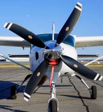 Front view of a Cessna 206H airplane parked on an airstrip under clear blue sky.