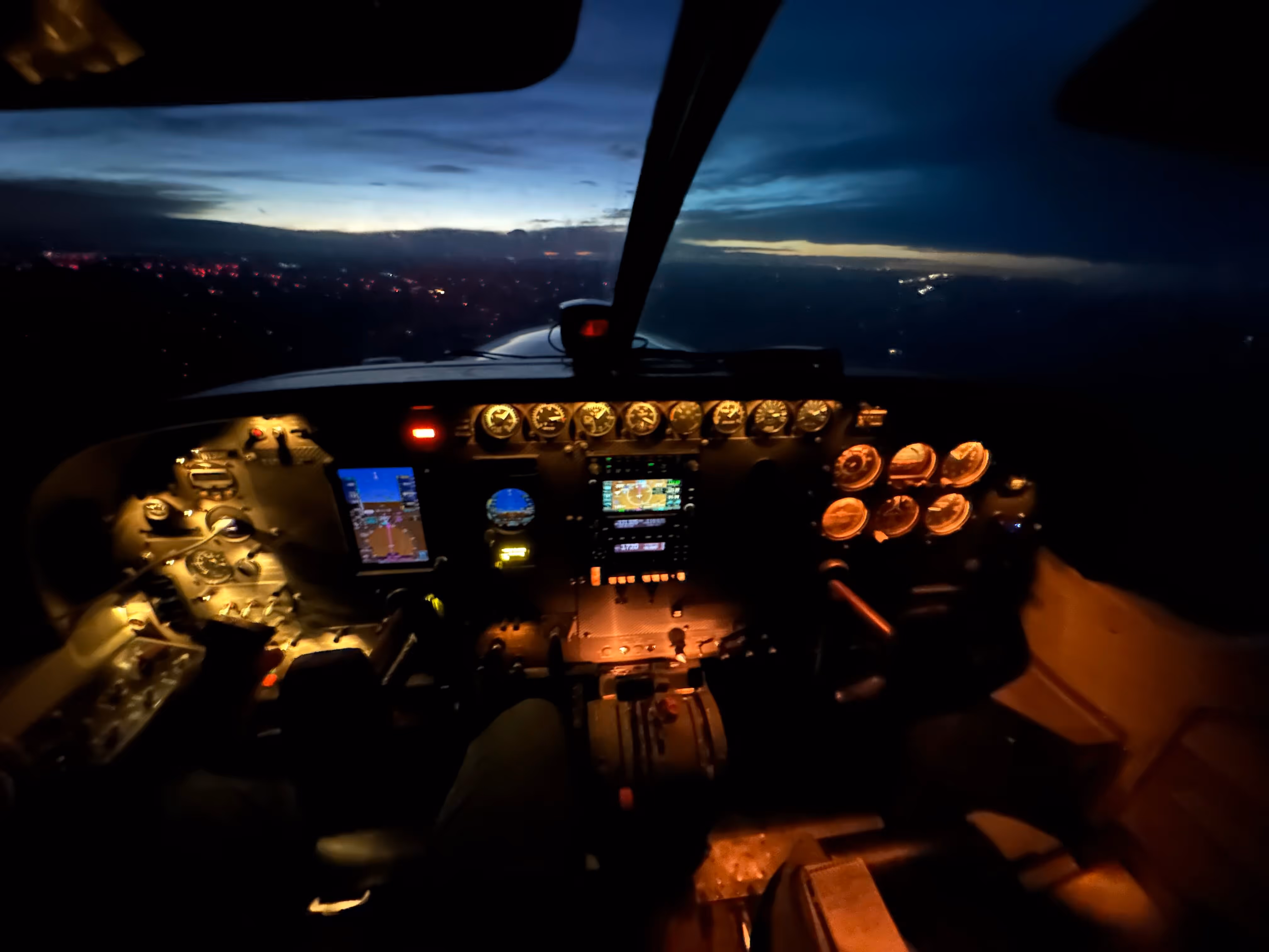 Illuminated Cessna Caravan cockpit at dusk with visible flight instruments and a darkening sky outside.