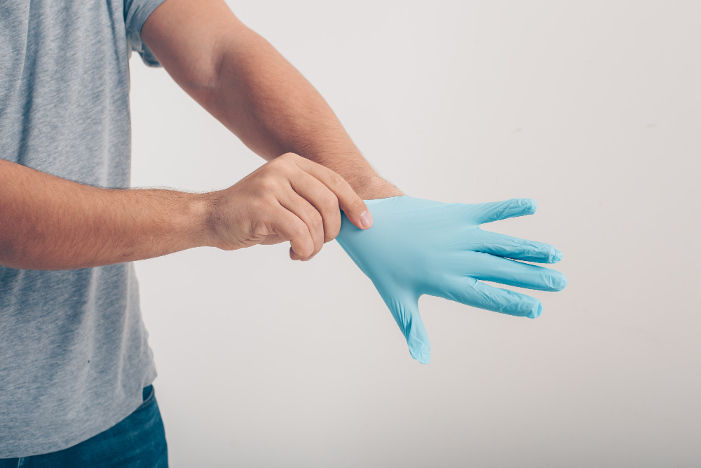Person wearing a blue disposable glove on their right hand against a plain background.