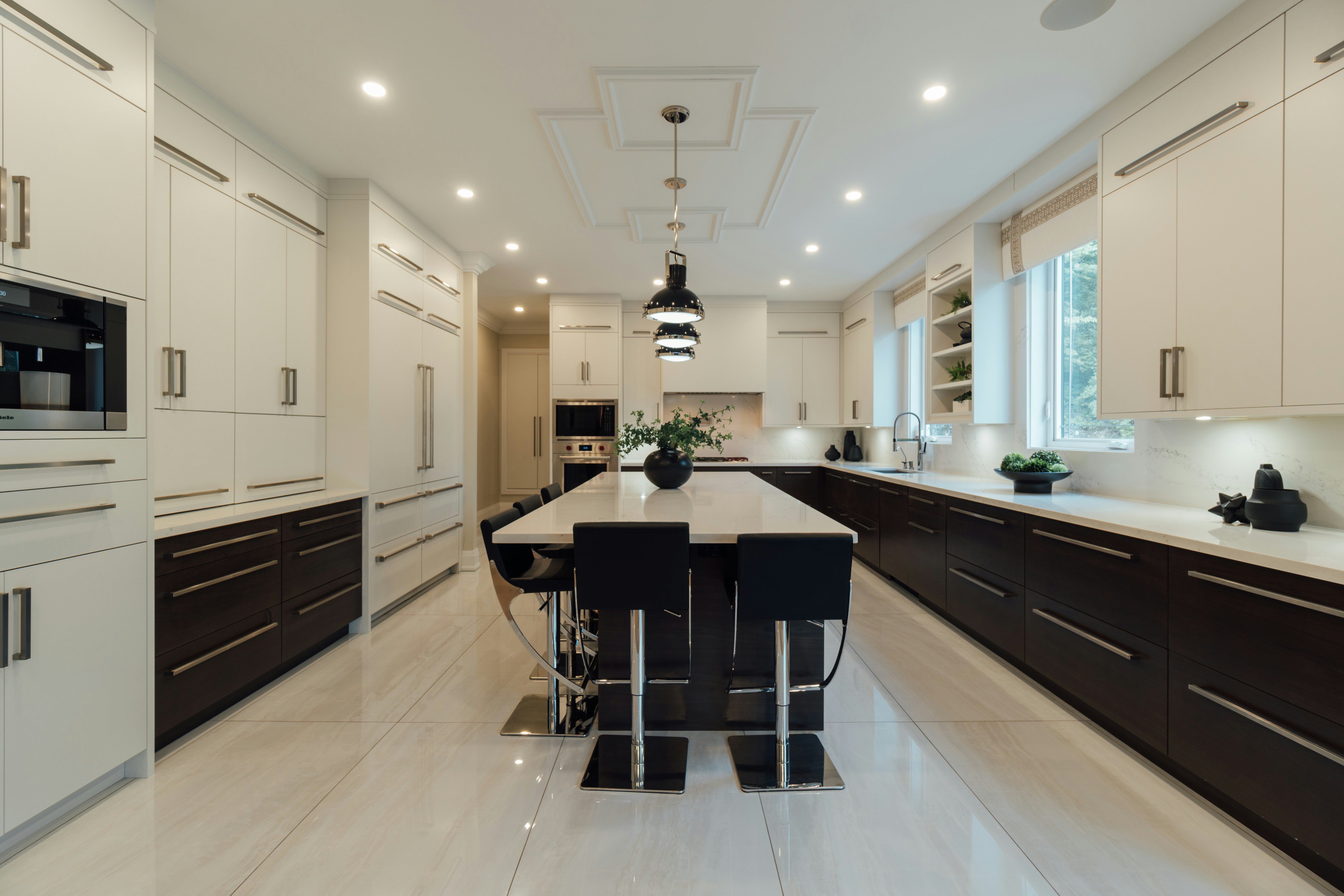 Modern kitchen with dark lower cabinets, white upper cabinets, large center island with marble countertop, black bar stools, and pendant lights.