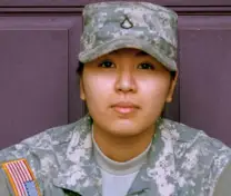 Portrait of a person in a digital camouflage military uniform and cap with a U.S. flag patch on the shoulder.
