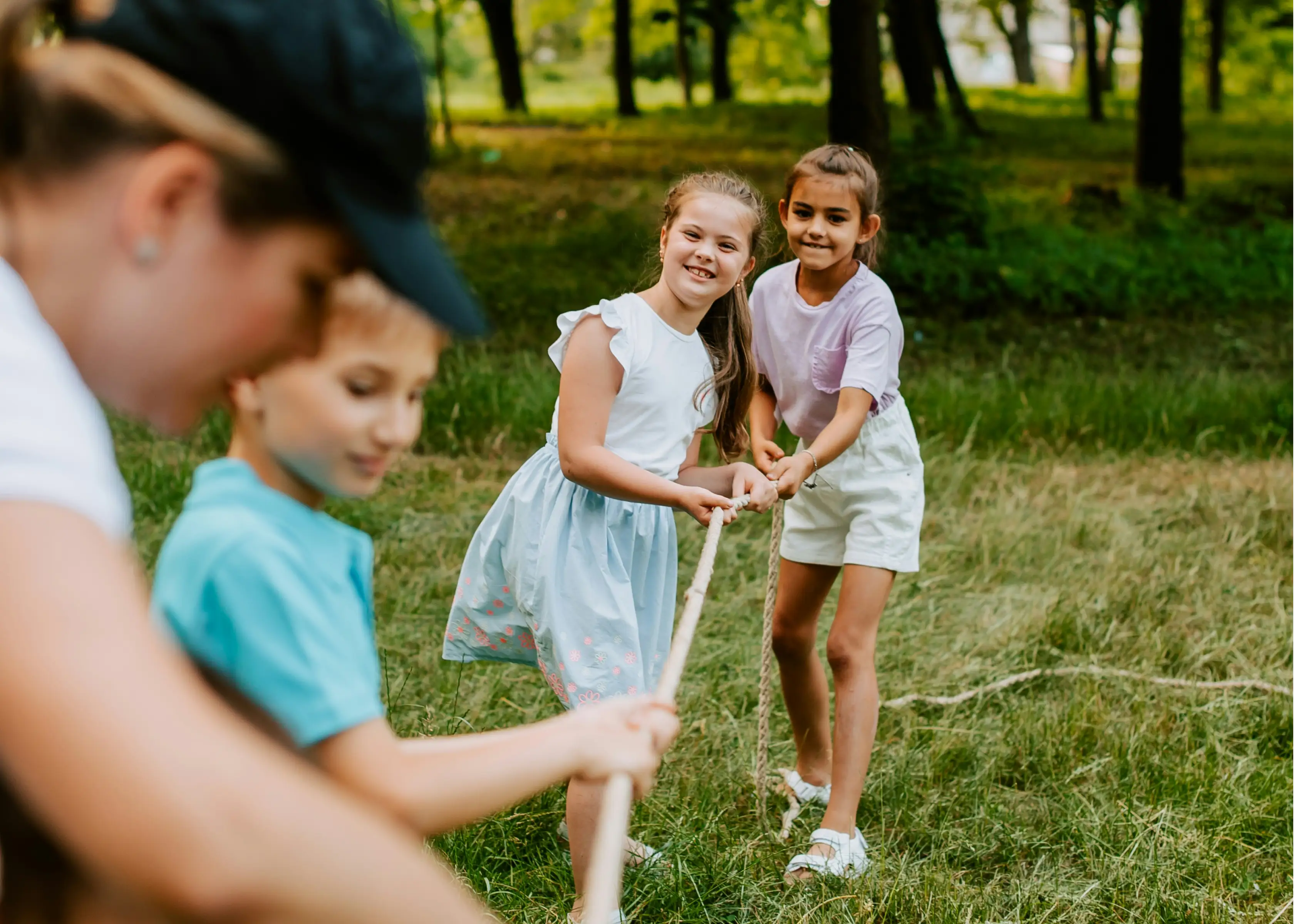 Two girls smiling and playing tug-of-war with a rope outdoors in a grassy area.