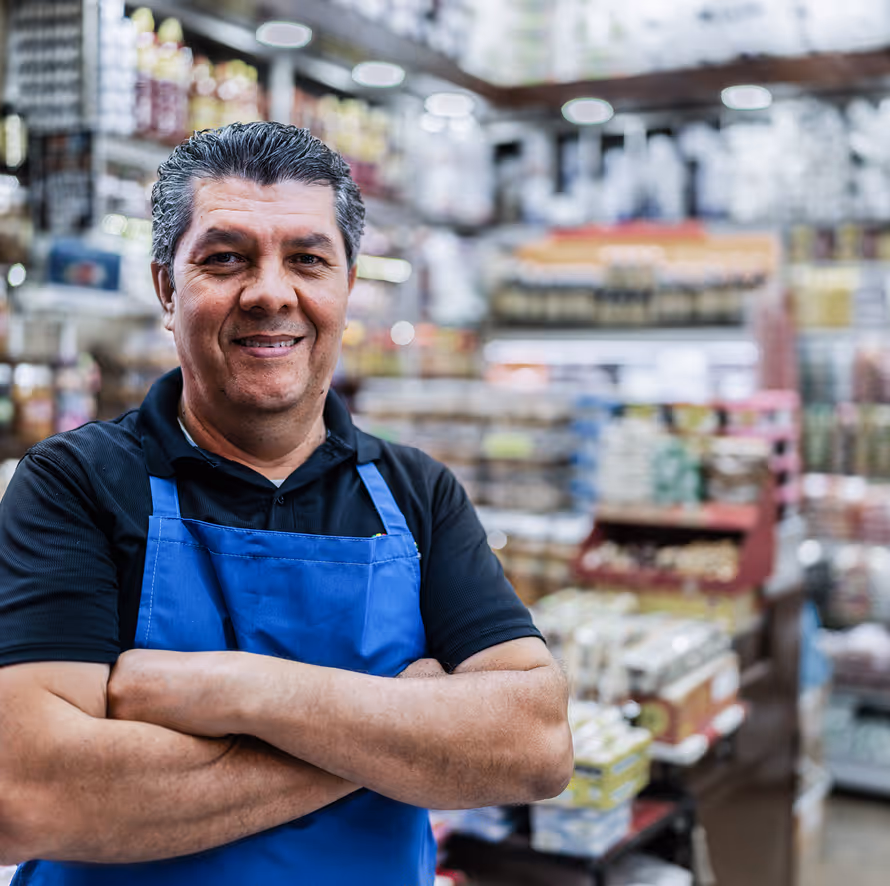 Elderly man with a beard and receding hairline wearing a salmon-colored button-up shirt sitting outdoors on a bench.
