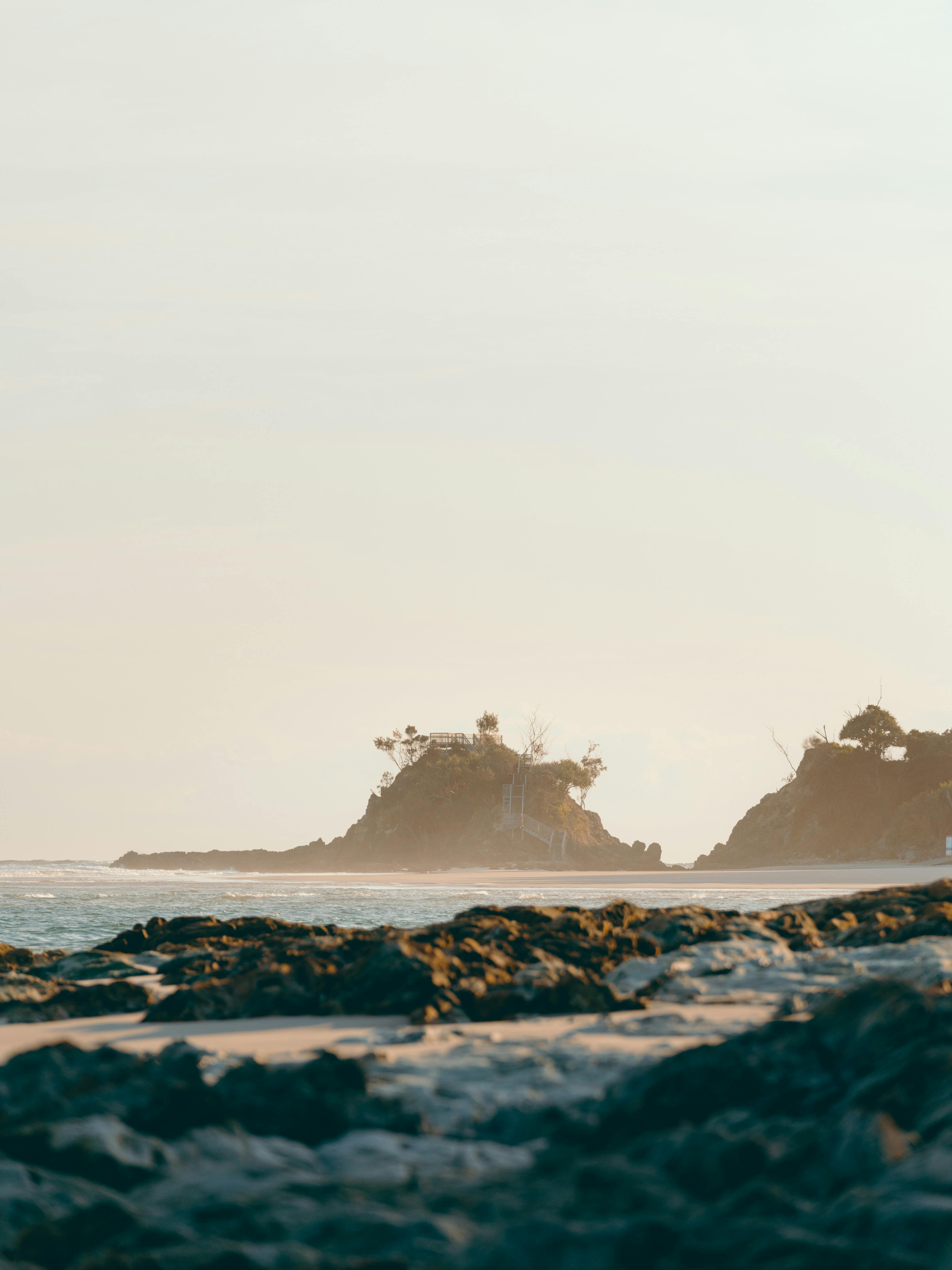 Rocky beach shoreline with a small tree-covered hill and a wooden staircase leading up to a lookout.