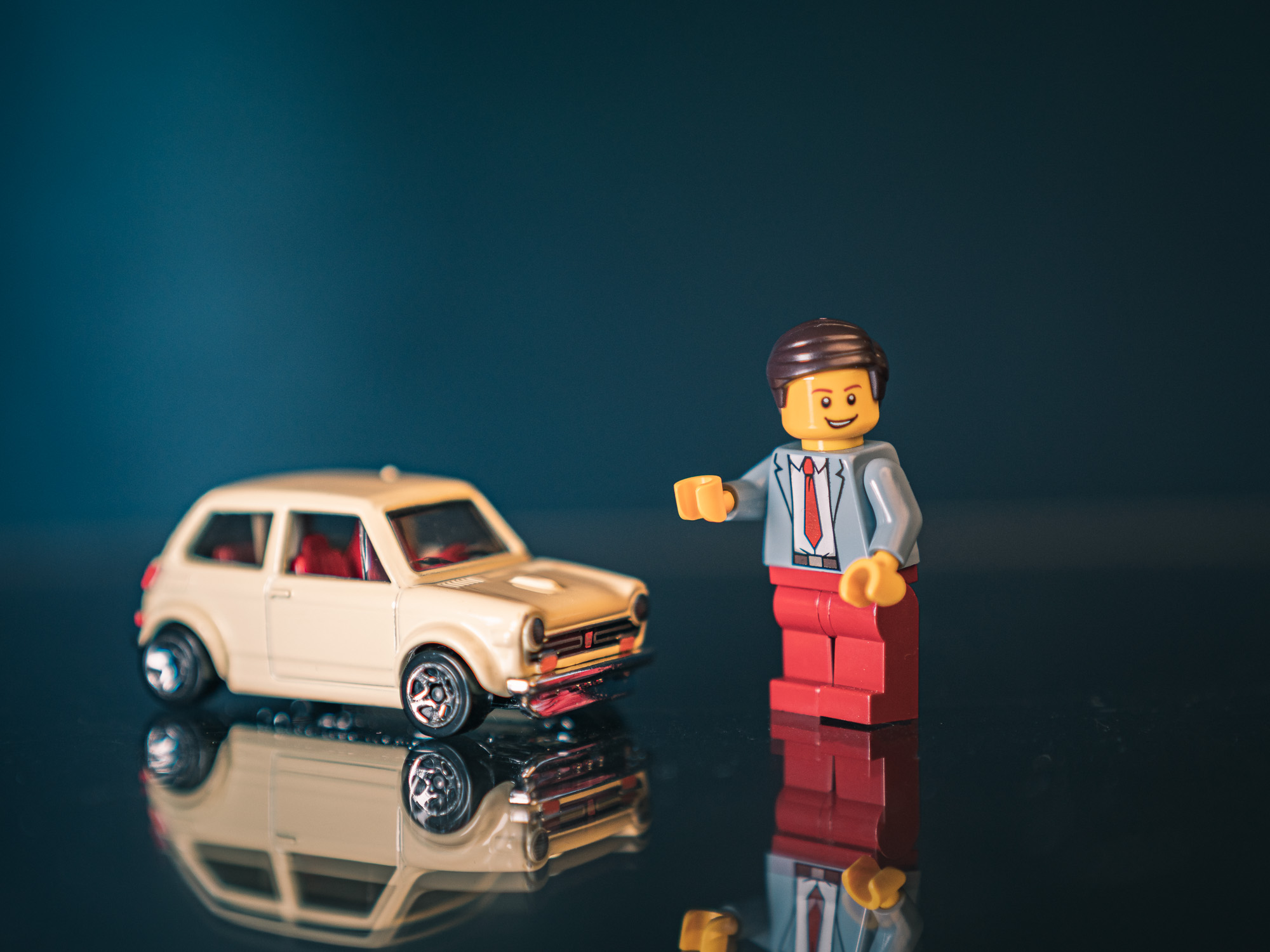 Toy car and minifigure reflected on a glossy blue surface
