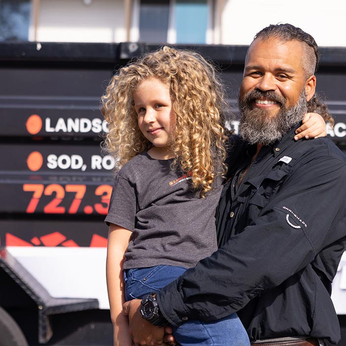 Now: Christopher holding his daughter beside a Sure Shot Property Enhancement Services vehicle.