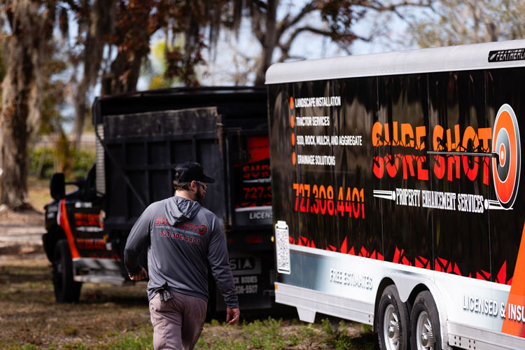 Sure Shot team member walking beside branded company vehicles and equipment at a project site