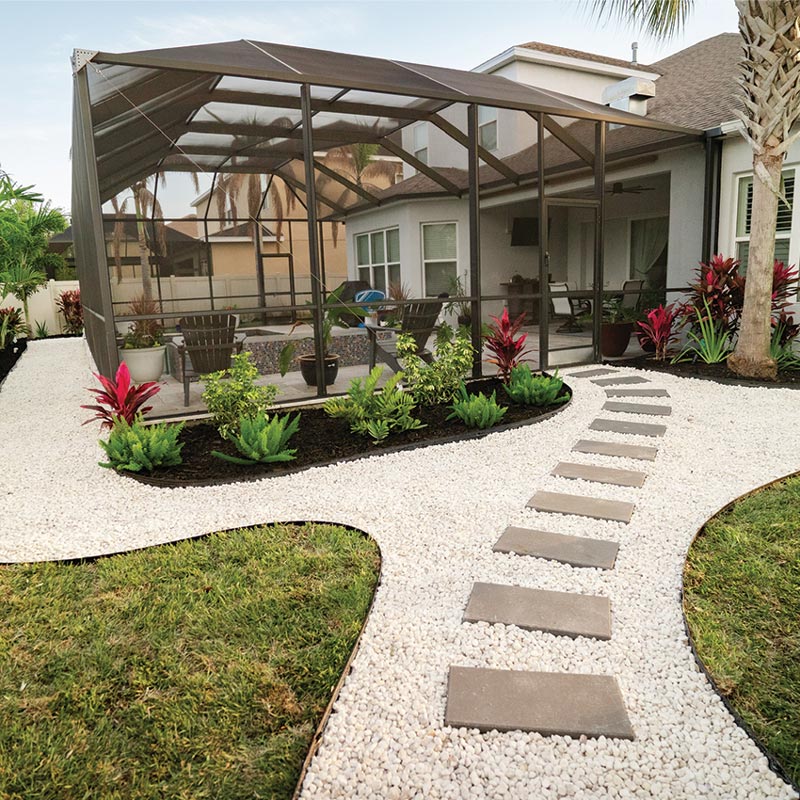 Backyard after landscaping with white decorative stone, stepping stones, tropical plants, and refreshed beds around the screened patio.