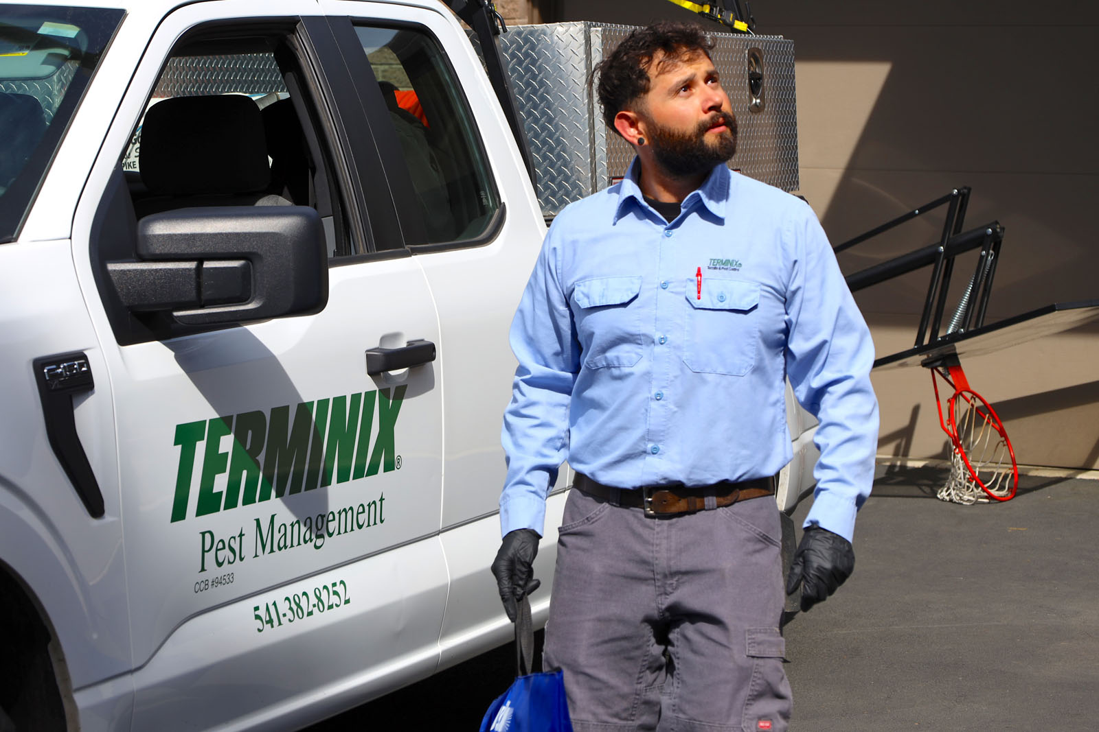 A Terminix technician is walking to his truck and looking at something high and out of the reader's view.
