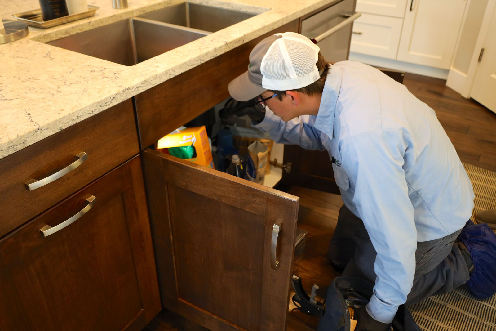 A Terminix technician is looking in the cabinet beneath the kitchen sink.