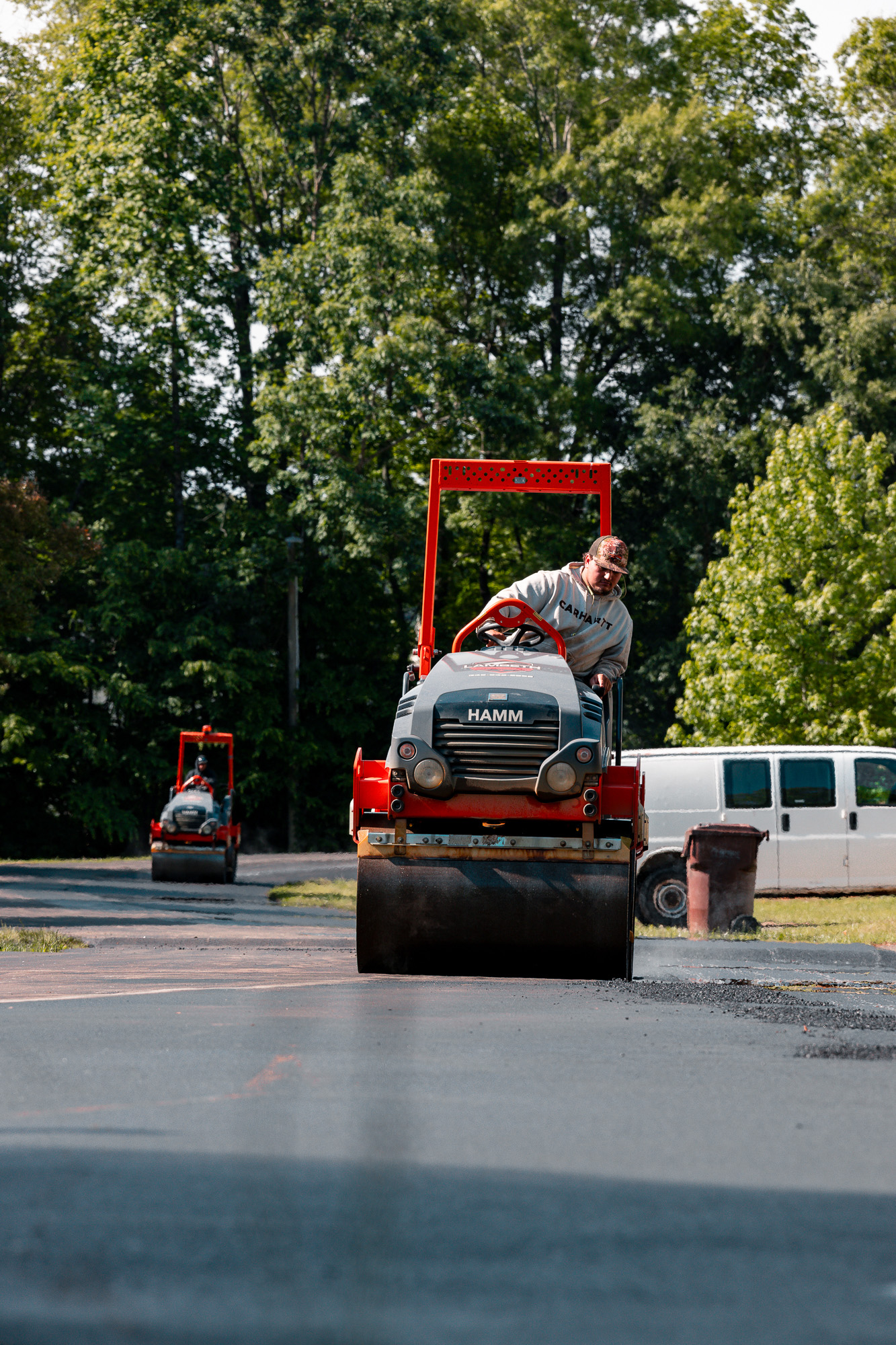 Three workers in lambeth high-visibility vests securing construction machinery on a flatbed truck in a parking lot.