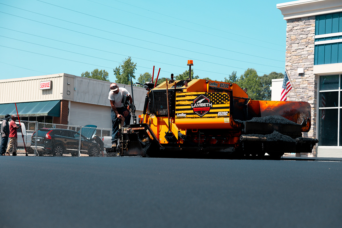 Lambeth Asphalt LeeBoy 8520C paver laying fresh asphalt in a commercial parking lot in Greensboro NC with crew member operating controls