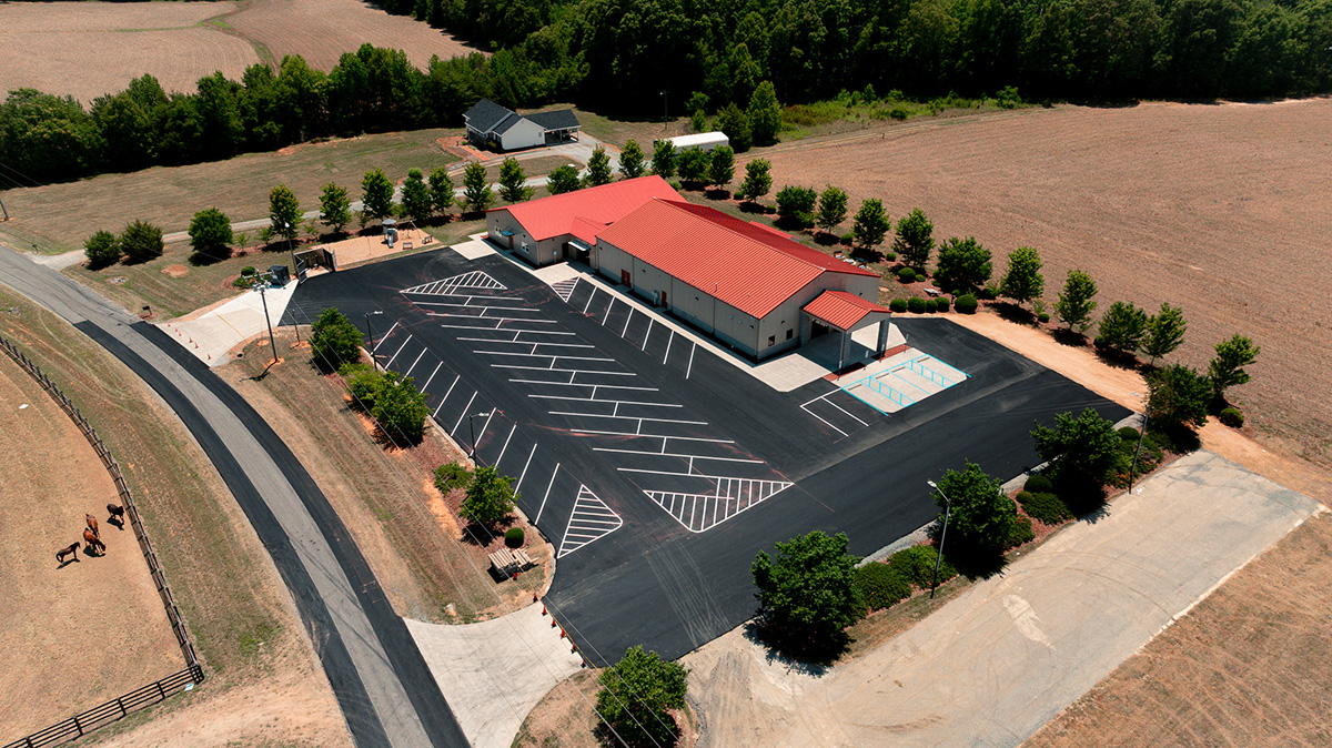 Aerial view of completed parking lot paving and striping at Reedy Fork Community Church in Browns Summit NC with horses visible in adjacent pasture